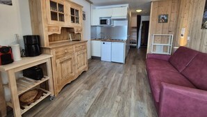 A compact kitchen with wooden cabinets, a microwave, and a dishwasher. There is a red sofa and a small table with a coffee maker. - 100m from resort center, Ground floor, tv, ski locker, 29m², Tignes (Tignes)