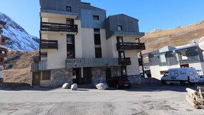 A multi-story building with balconies, a sign reading "Le Plein Soleil," and a parking area with a van and logs. - 100m from resort center, Ground floor, tv, ski locker, 29m², Tignes (Tignes)