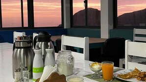 A breakfast table with a view of a sunset, including a thermos, milk, juice, bread, and bananas. - The Retreat (Ribeira Grande)