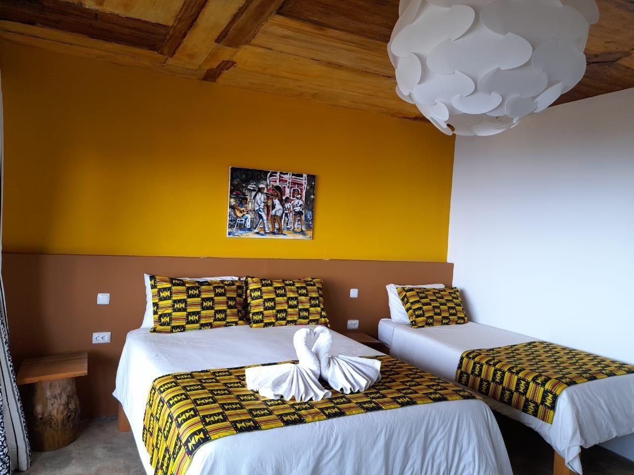 A hotel room with two beds, a wooden ceiling, a yellow wall, and a painting above the beds.