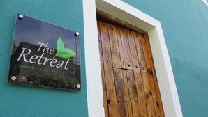 A wooden door with a metal handle and a sign above it that reads "The Retreat" with a green leaf logo. - The Retreat (Ribeira Grande)