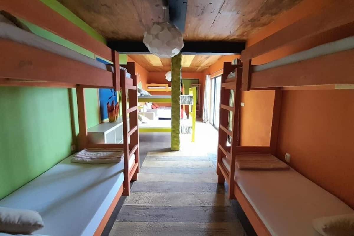 Um vagão de trem com beliches de madeira, paredes verdes e laranja, e um corredor central.