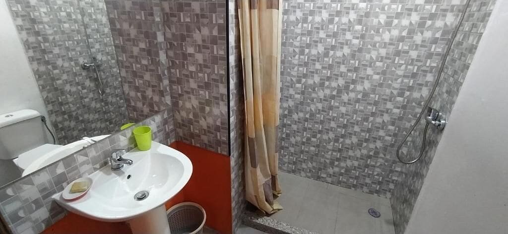 A bathroom with a white sink, a mirror, and a shower area with a tiled wall.