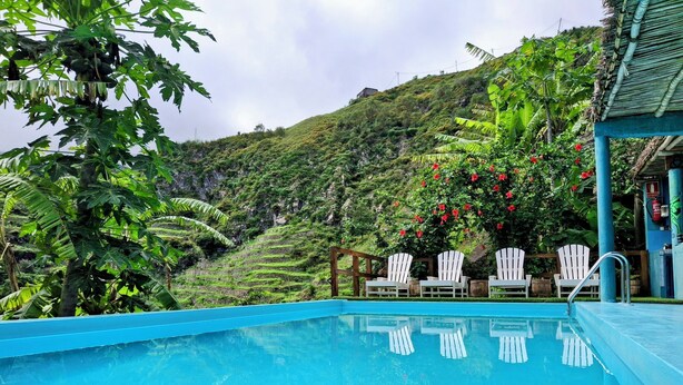 A swimming pool with white chairs and a view of a lush green hillside. - The Retreat (Ribeira Grande)