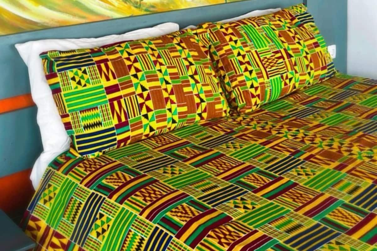 Cama com colcha e almofadas estampadas, pintura abstrata vibrante na parede, e parede com destaque em azul.