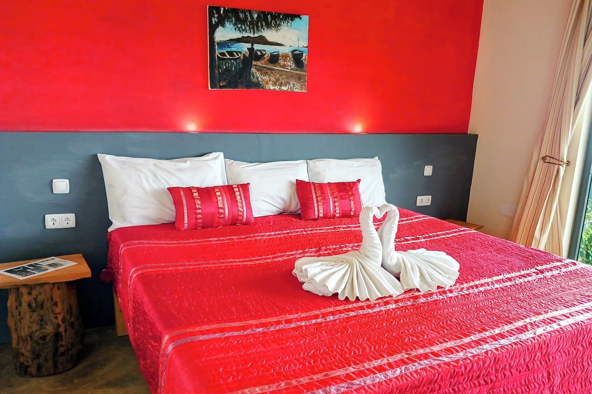 Quarto de hotel com colcha vermelha, almofadas brancas e toalhas dispostas em formato de cisne.