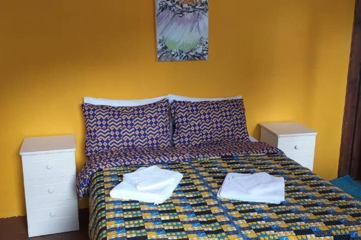 Uma cama com roupa de cama estampada, duas mesas de cabeceira e uma obra de arte na parede.