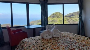 A hotel room with a bed, a red chair, and a view of green hills and the sea. - The Retreat (Ribeira Grande)