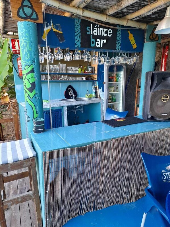 A tiki bar with a blue counter, shelves with bottles, and a sign that reads "slainte bar".