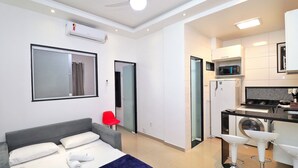 Une chambre d’hôtel moderne équipée d’un lit, d’un fauteuil rouge, d’une kitchenette et d’un lave-linge.