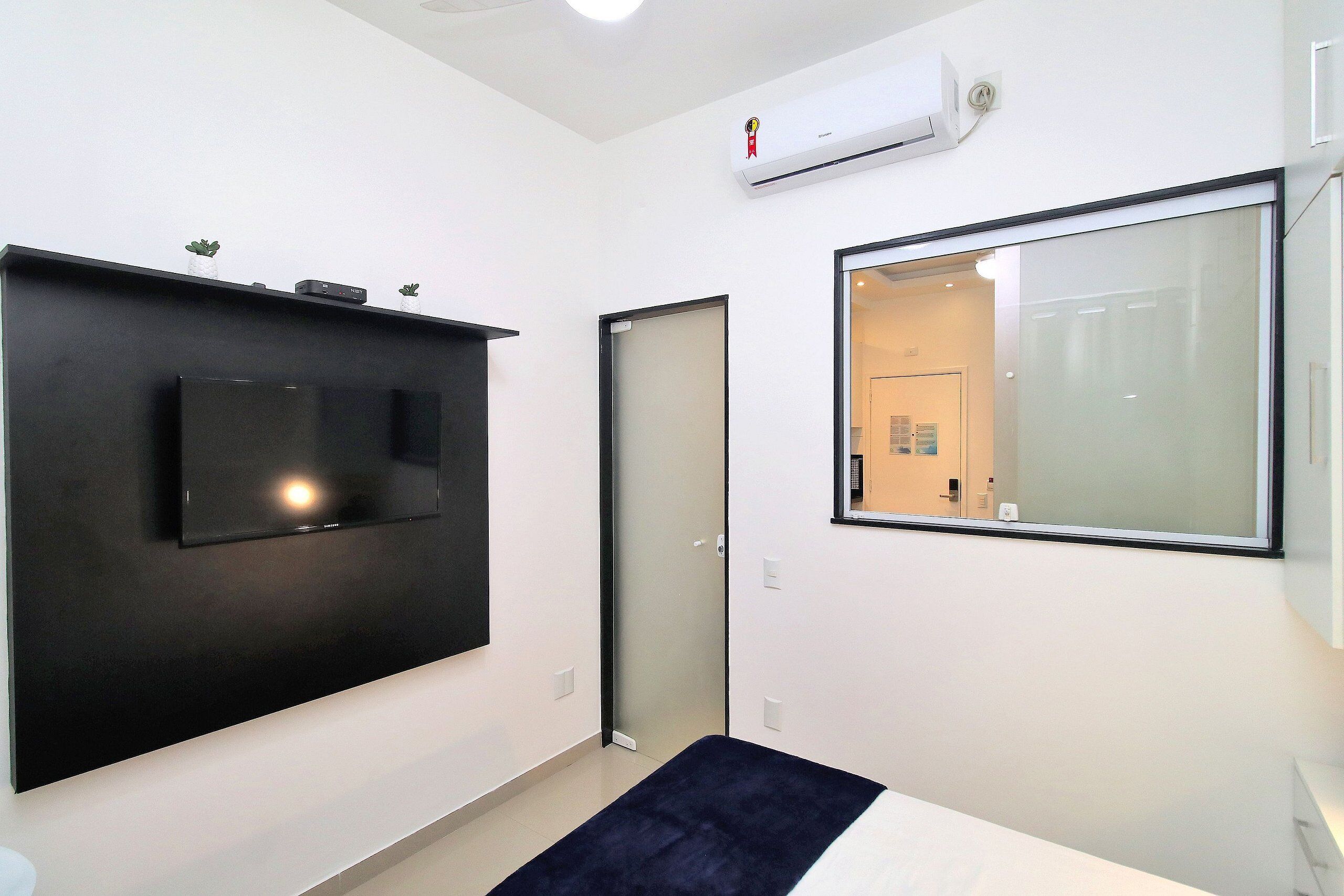 A modern hotel room with a flat-screen TV mounted on the wall, a large mirror, and a sliding door leading to the bathroom.