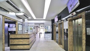 Un hall d’entrée propre et moderne, avec un comptoir d’accueil, des ascenseurs et des panneaux d’information.