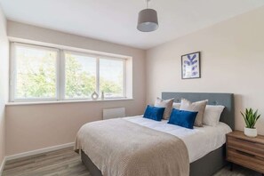 Un dormitorio con cama, mesitas de noche, ventana con persianas, lámpara colgante y un cuadro en la pared.