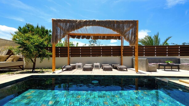 Een zwembad met een houten pergola en ligbedden.