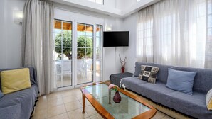 Een moderne woonkamer met een glazen salontafel, een grijze bank, een geel kussen en een aan de muur bevestigde televisie.