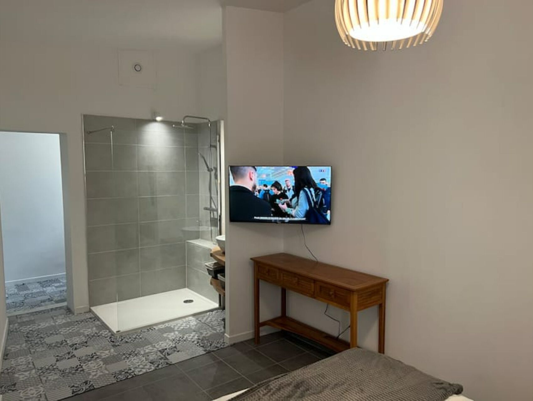 Ein modernes Badezimmer mit Dusche, Toilette und Waschbecken. Ein Fernseher ist an der Wand montiert und es gibt eine hölzerne Bank.