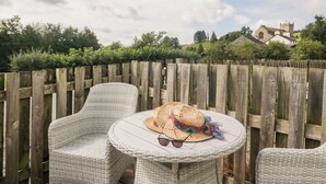 A wicker chair and table set outdoors with a wooden fence and greenery in the background. - Betty's Loft (Ambleside)