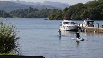 A calm lake with boats docked at a pier, surrounded by lush greenery and mountains in the background.