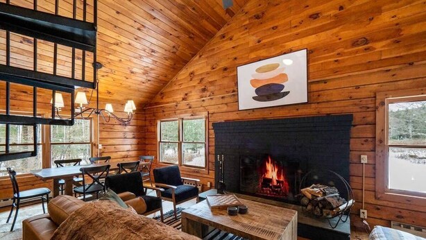 A cozy cabin interior with a fireplace, wooden walls, and a dining area. - Quiet Cabin On Over 12 Acres Of Woods! (Becket)