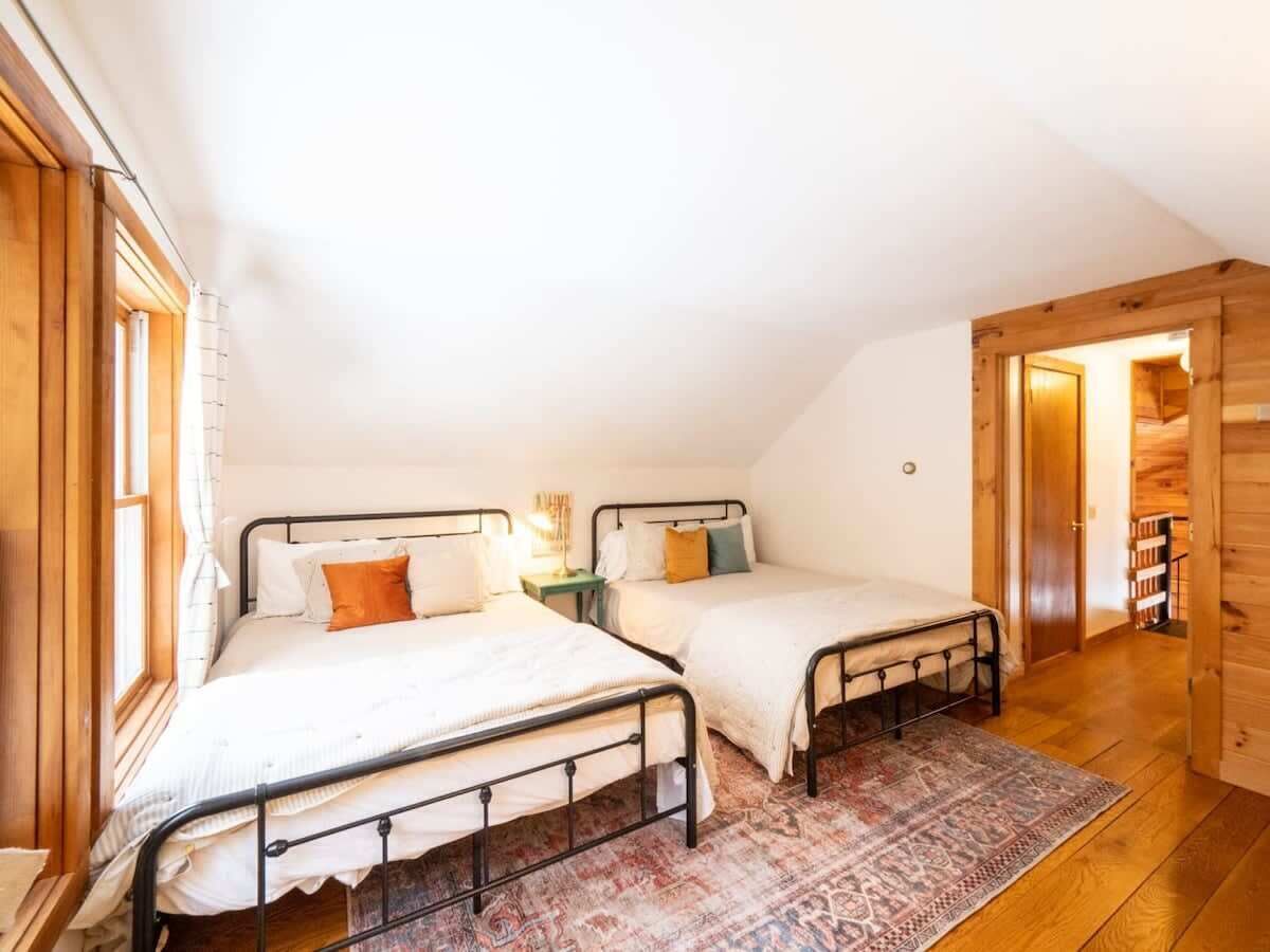 A cozy attic bedroom with two metal beds, a patterned rug, and wooden walls.