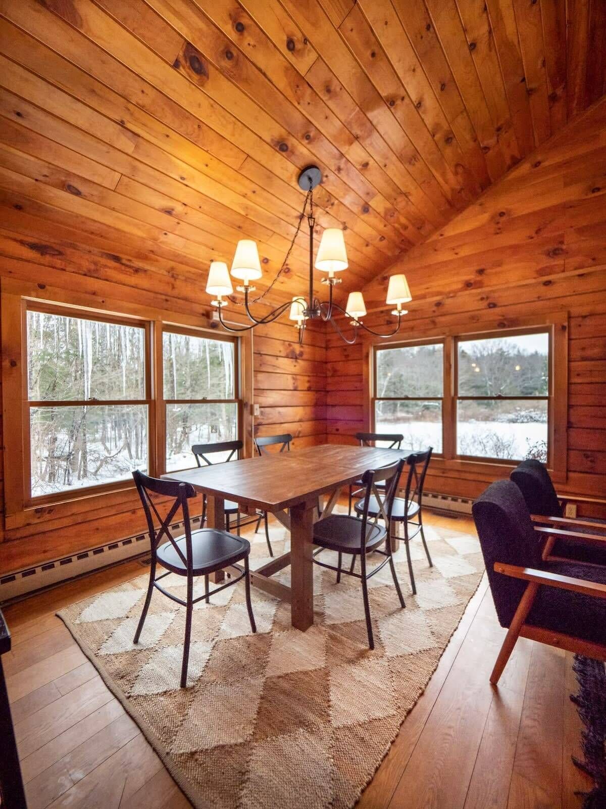 L’intérieur d’un chalet en bois, avec une table à manger, des chaises et un lustre.