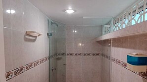 Een badkamer met een douchecabine van glas, een toilet en een plankje met een zakdoosje.