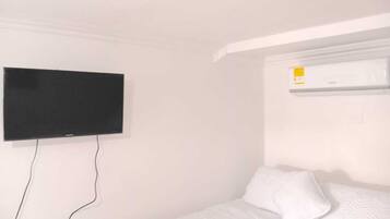 A room with a bed, a flat-screen TV mounted on the wall, and an air conditioning unit.