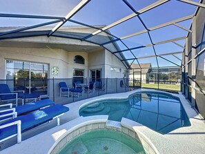 A covered outdoor pool area with lounge chairs and a hot tub.