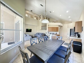 A spacious living area with a dining table, chairs, and a kitchen in the background.