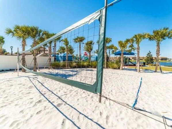 Ein Beachvolleyballfeld mit Netz, Palmen und blauem Himmel.