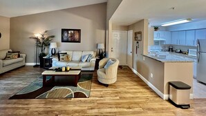 A spacious living room with a sofa, coffee table, and a dining area with a kitchen in the background.