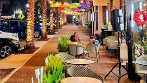 An outdoor seating area with tables and chairs, palm trees, and string lights.