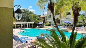 A swimming pool surrounded by palm trees and lounge chairs, with a building in the background.
