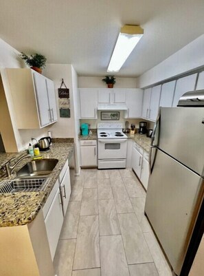Kitchen features a stainless steel refrigerator, white stove, and single sink with faucet.