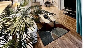 A spacious living area with a large TV, a dining table, and a kitchen in the background.