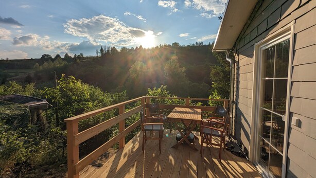 A wooden deck with a table and chairs, overlooking a forested area with a clear sky. - Hellaberg III: Quiet vacation home with sauna on the edge of the forest (Schleusegrund)