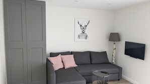 A modern living room with a grey sectional sofa, a small round side table, a lamp, and a framed deer illustration on the wall. - Hellaberg III: Quiet vacation home with sauna on the edge of the forest (Schleusegrund)
