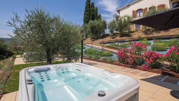 Una vasca idromassaggio in un'area esterna curata con giardino e vista su una casa.