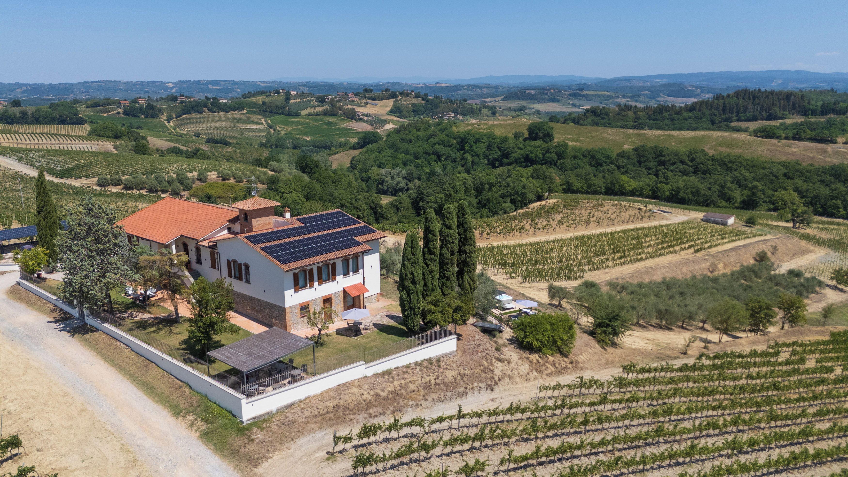 Ein Haus mit einer Solaranlage auf dem Dach, umgeben von Weinbergen und einer hügeligen Landschaft.