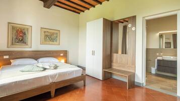A bedroom with a wooden bed, white wardrobe, and a bathroom visible through an open door.