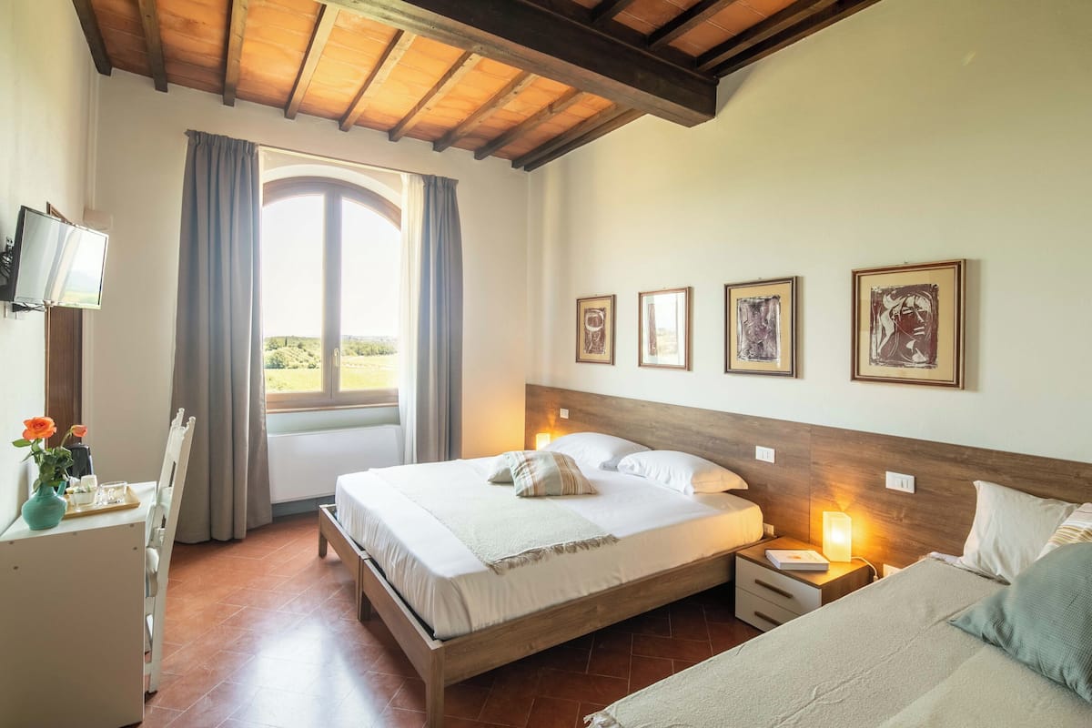 A bedroom with a wooden bed, bedside tables, a TV, and a window with curtains.
