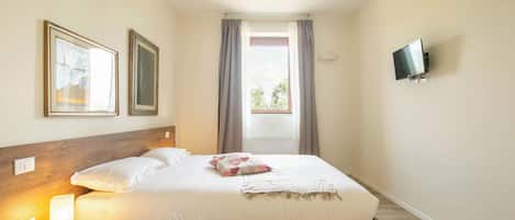 A neatly made bed with a wooden headboard, a bedside table with a lamp, and a television mounted on the wall.