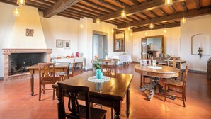 A spacious dining area with wooden tables and chairs, a fireplace, and hanging pendant lights. - Podere La Quercia (San Gimignano)