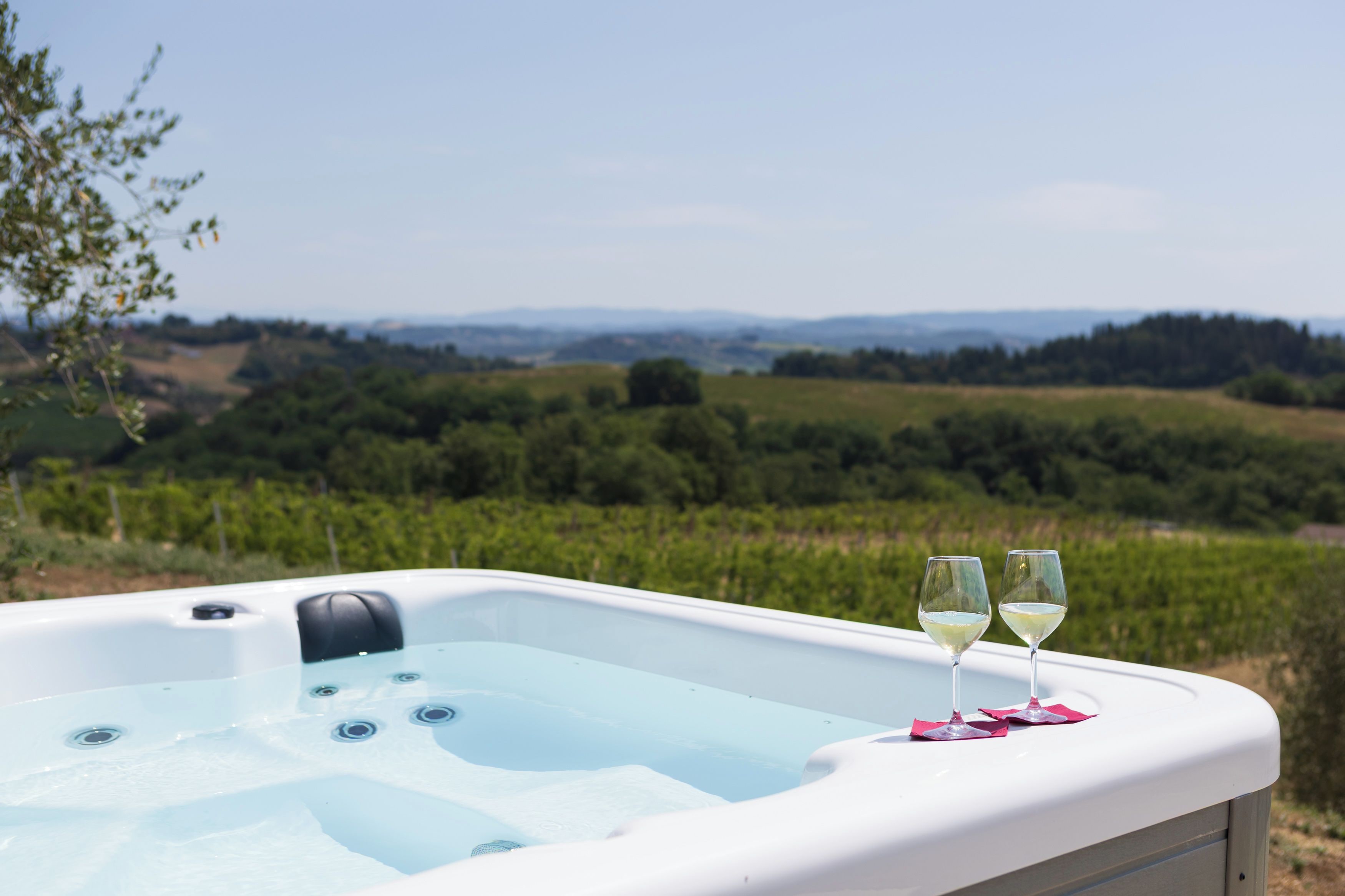 Un bain à remous avec deux verres de vin blanc posés sur une table, le tout sur fond de vignoble et de collines ondoyantes.