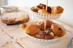 A tray of assorted pastries and a cake on a table with a lace tablecloth. - Podere La Quercia (San Gimignano)