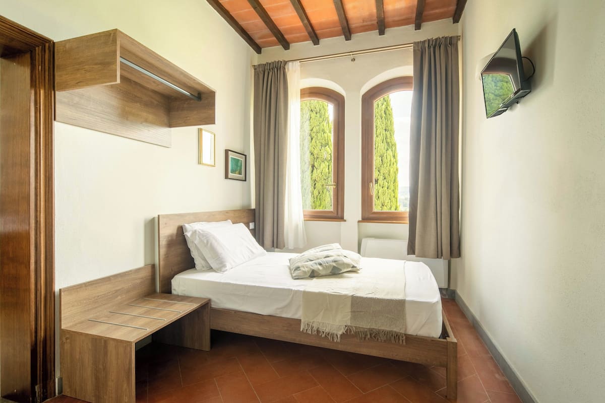 A single bed with a wooden headboard, a bedside table, and a TV mounted on the wall.