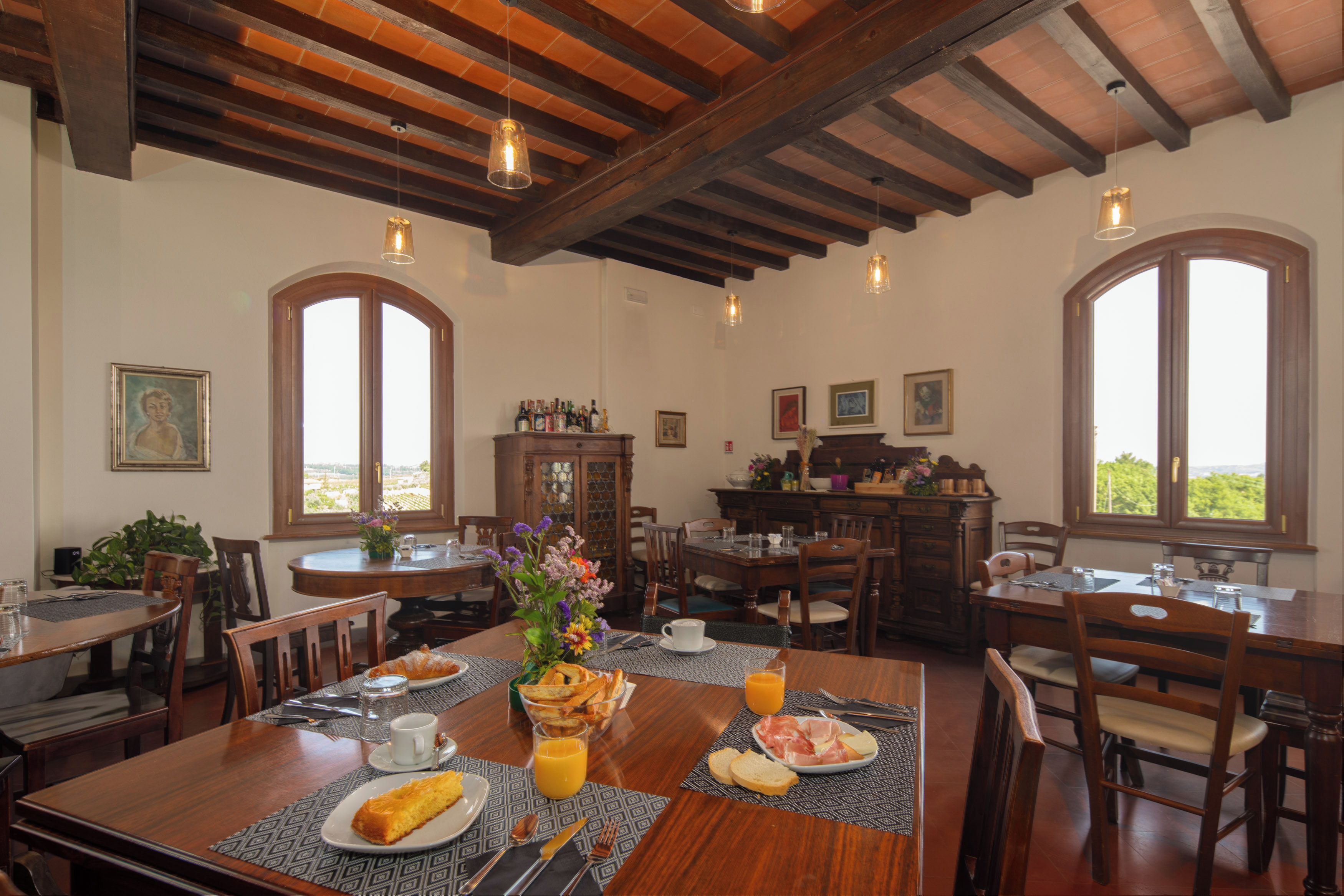 Zona pranzo con tavoli e sedie di legno, un buffet con cibo e bevande, e ampie finestre con vista.