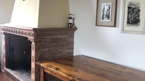 A room with a brick fireplace, a wooden table, and two framed pictures on the wall. - Podere La Quercia (San Gimignano)