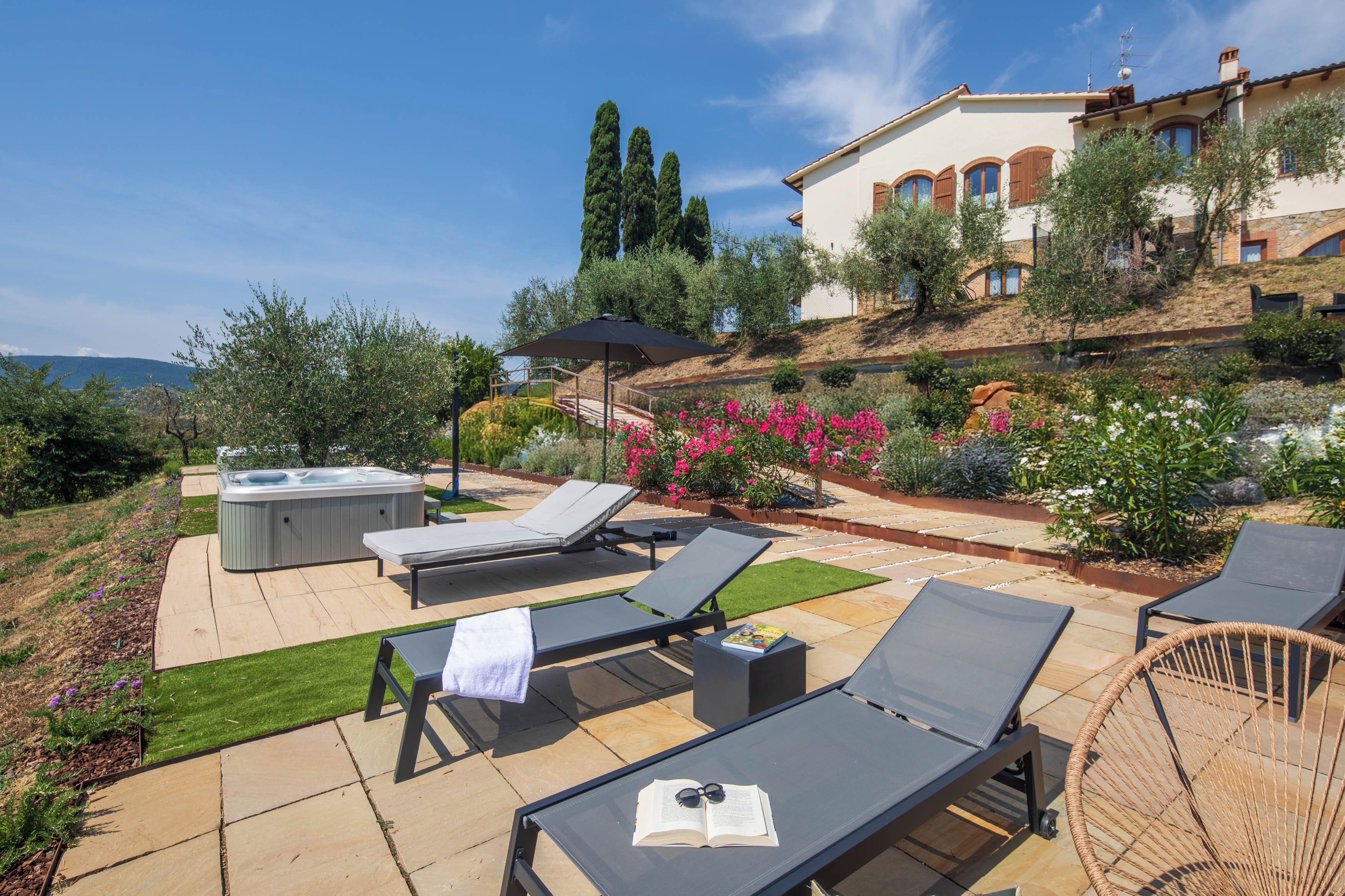 A patio with lounge chairs, a hot tub, and a view of a hillside with a house.