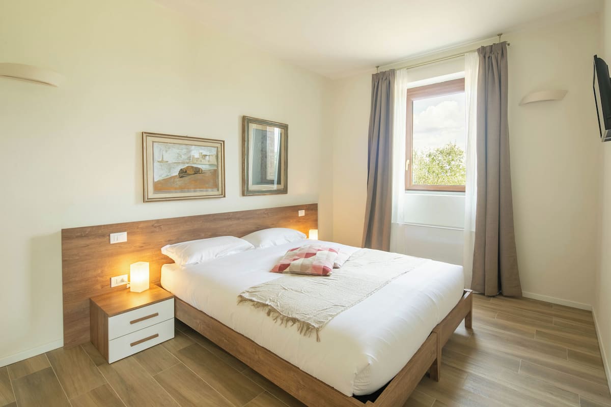 A neatly made bed with a wooden headboard, a bedside table with a lamp, and two framed pictures on the wall.